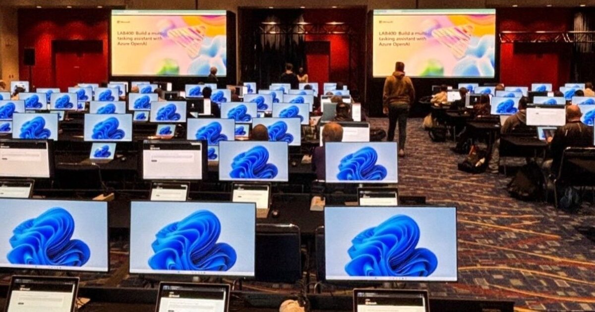 Ein Konferenzraum mit sehr vielen Arbietsplätzen und Monitoren; einige Menschen sitzen an den Arbietsplätzen und schauen auf die Monitore