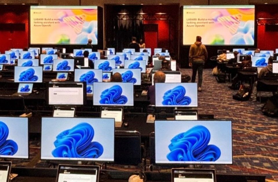 Ein Konferenzraum mit sehr vielen Arbietsplätzen und Monitoren; einige Menschen sitzen an den Arbietsplätzen und schauen auf die Monitore