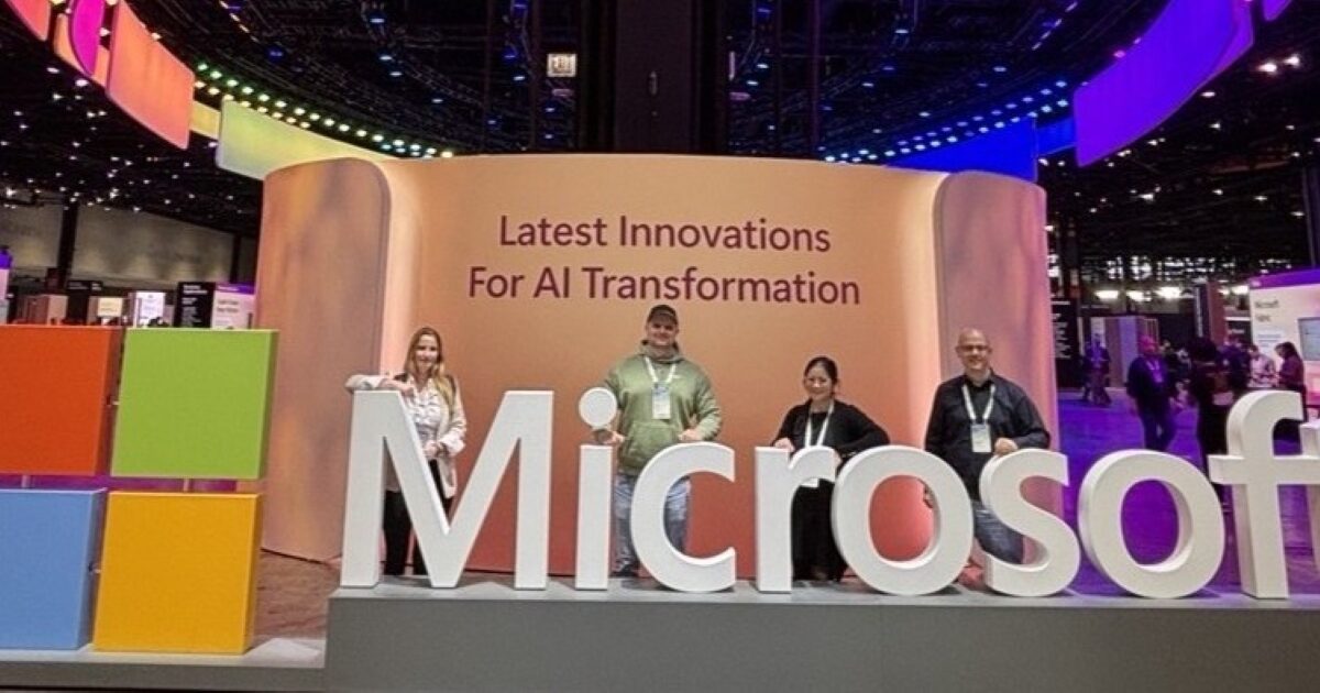 Vier Mitarbieterinnen und Mitarbeiter stehen hinter einem großen Microsoft Slogan und vor eine rWand mit der Aufrsicht