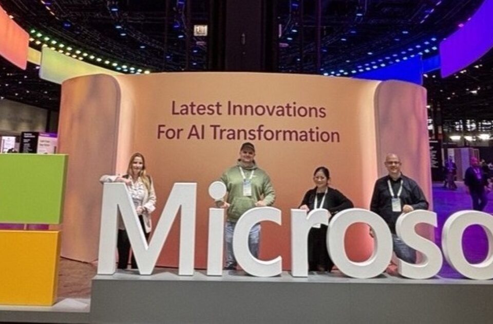 Vier Mitarbieterinnen und Mitarbeiter stehen hinter einem großen Microsoft Slogan und vor eine rWand mit der Aufrsicht