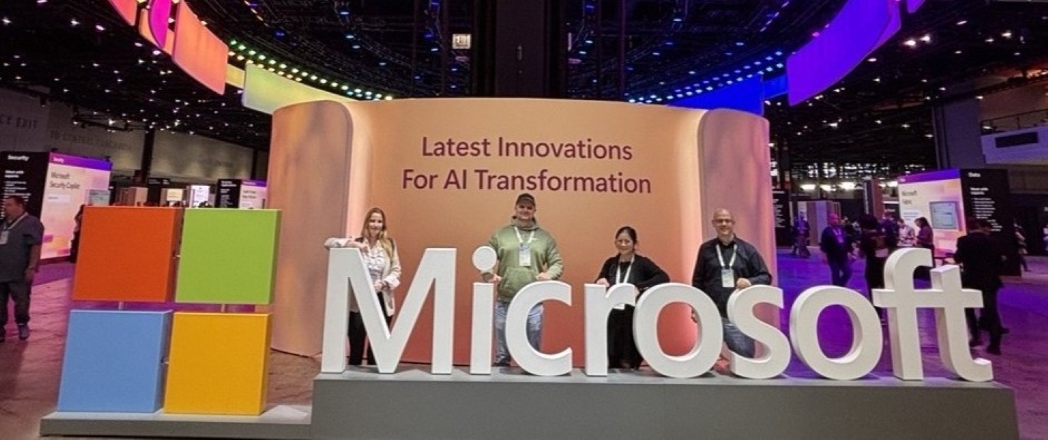 Vier Sven Mahn IT Mitarbeiterinnen und Mitarbeiter stehen hinter einem großen Microsoft-Slogan auf der Microsoft Ignite 2024